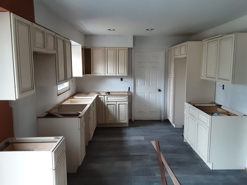 Kitchen under construction with cream cabinets, dark gray floor, and white door.