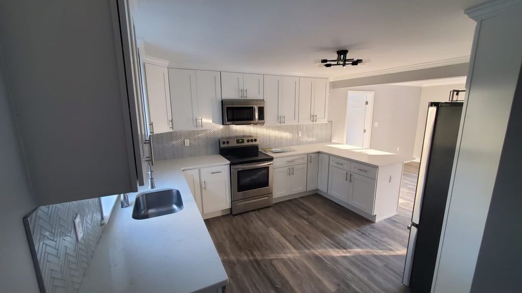 Bright, modern kitchen with white cabinets, stainless steel appliances, and wood-look flooring.