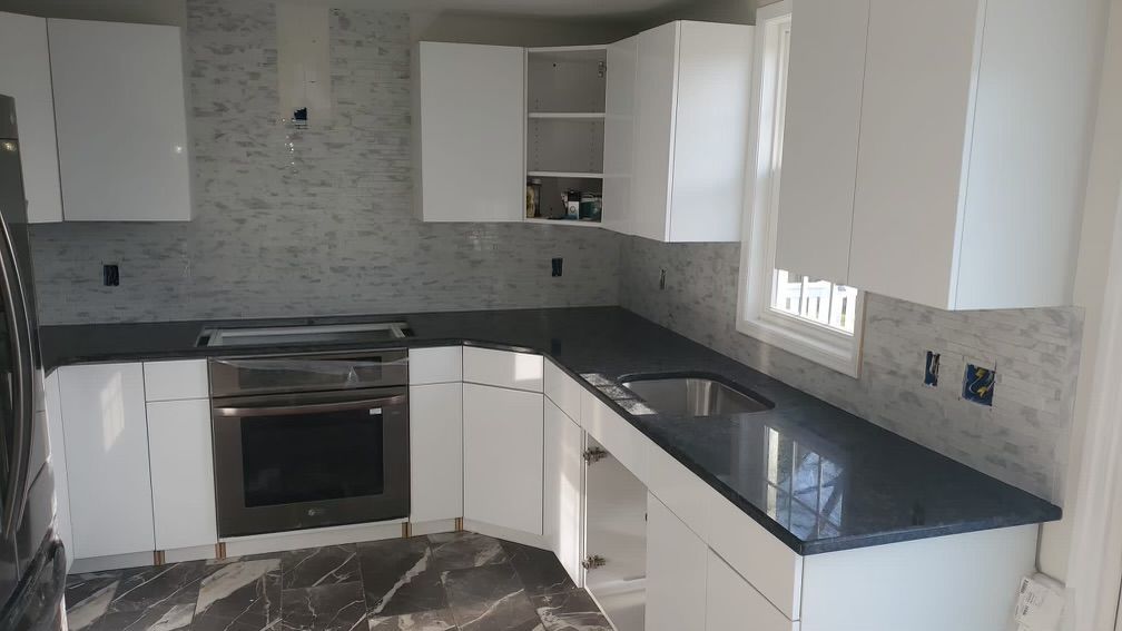 White kitchen cabinets with black countertop, stainless steel oven, gray backsplash.
