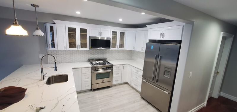 A modern kitchen with white cabinets, stainless steel appliances, and light countertops.