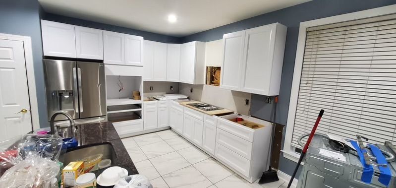A newly renovated kitchen with white cabinets and stainless steel appliances under construction.