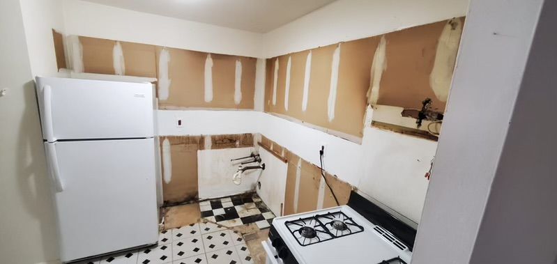 A small kitchen under renovation with exposed walls. White refrigerator and stove sit on a checkered floor.