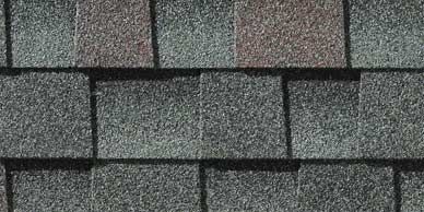Close-up of overlapping asphalt roof shingles in shades of gray, green, and brown.