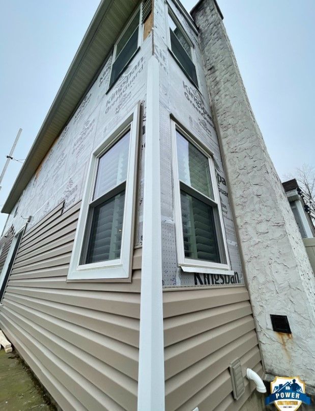 Exterior corner of a house with vinyl siding and windows. The upper portion has exposed sheathing.