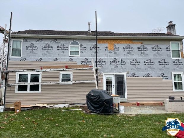 Back of a house with siding being installed, beige color, with a covered grill and scaffolding.