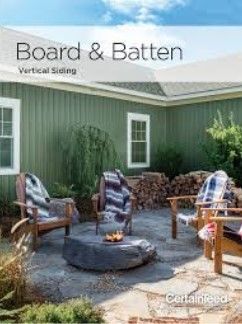 Green house with board & batten siding; outdoor patio with chairs, a fire pit, and woodpile.