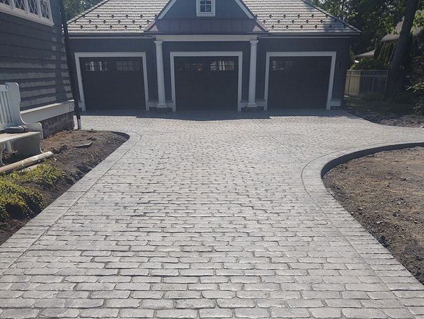 Driveway leading to a three-car garage. Driveway is paved with brick pattern concrete.