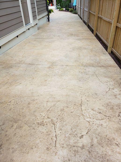 Concrete walkway with a textured surface, between a house and a wooden fence.