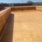 A low-angle view of a flat roof with tan-colored coating and brick-like walls.