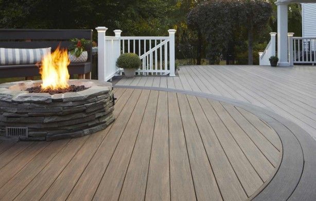 Stone fire pit with flames on a composite deck, leading to a white railing.