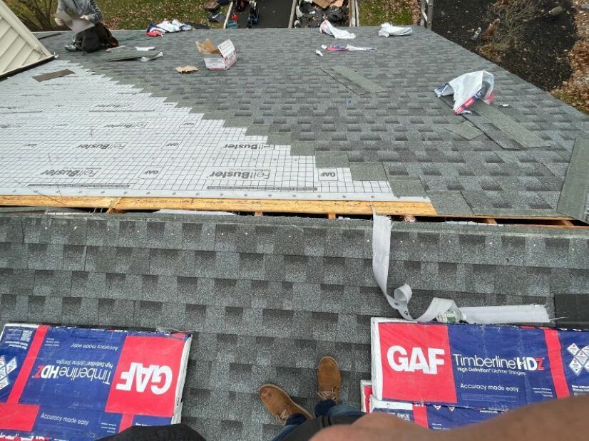Rooftop with GAF shingles; partially installed. White underlayment visible.  Brown shoes, debris, and tools scattered.