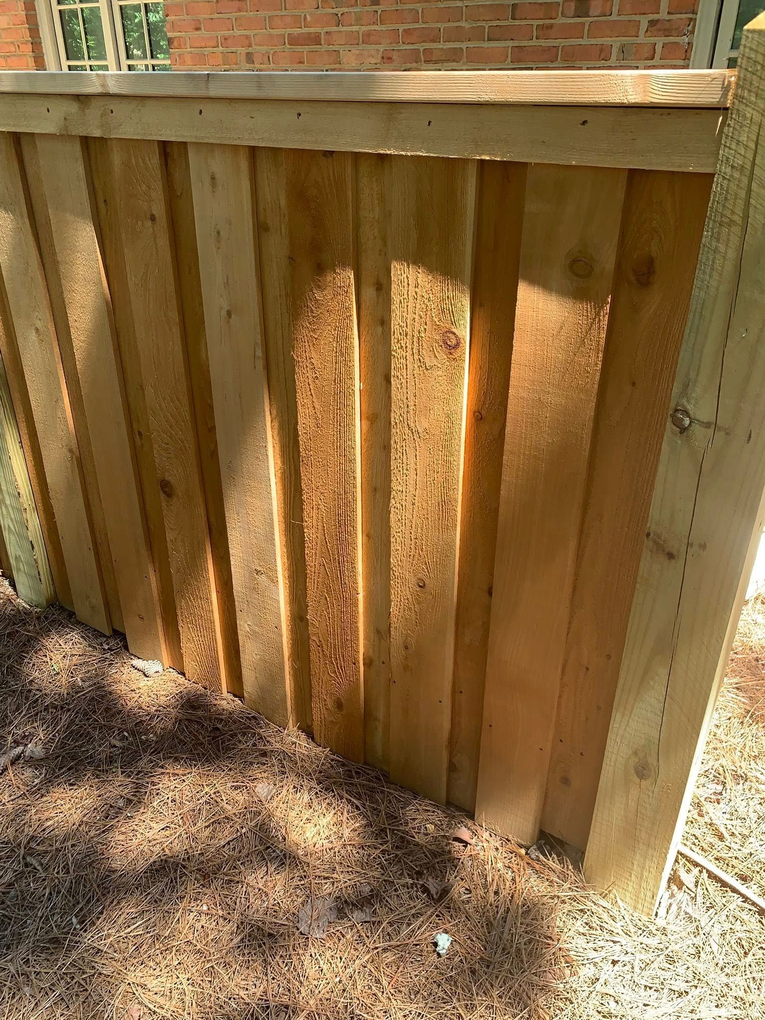 Wooden fence, vertical planks, against brick wall, set in gravel ground.