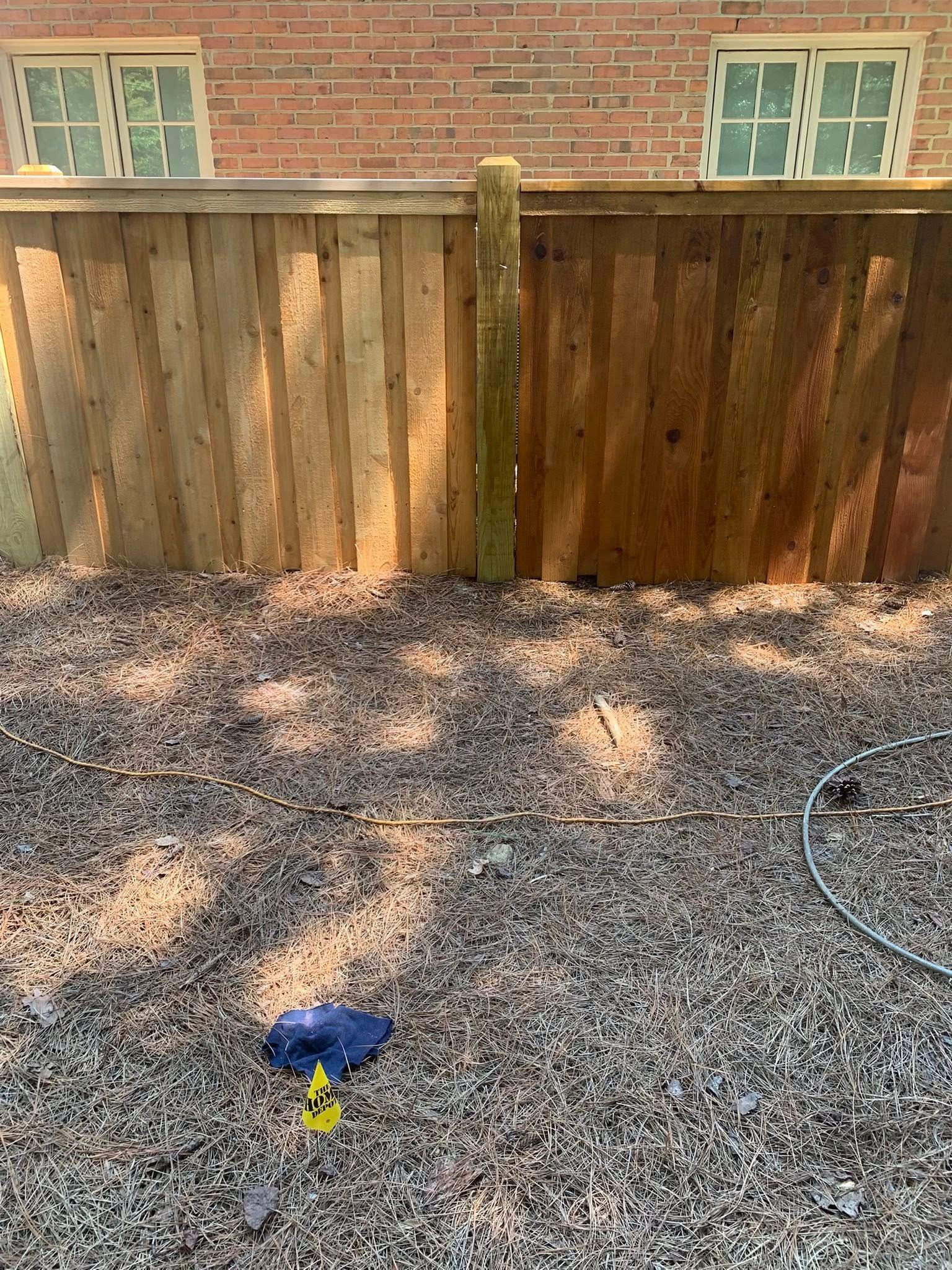 A wooden fence, half cleaned. Brown and tan planks. Gravel ground, brick building.