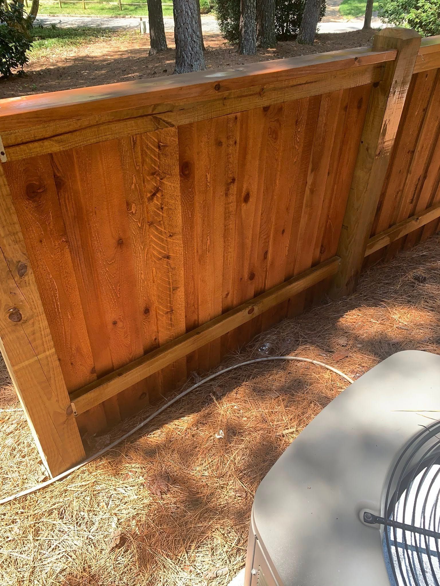 Wooden fence in backyard, next to an AC unit, on a sunny day.