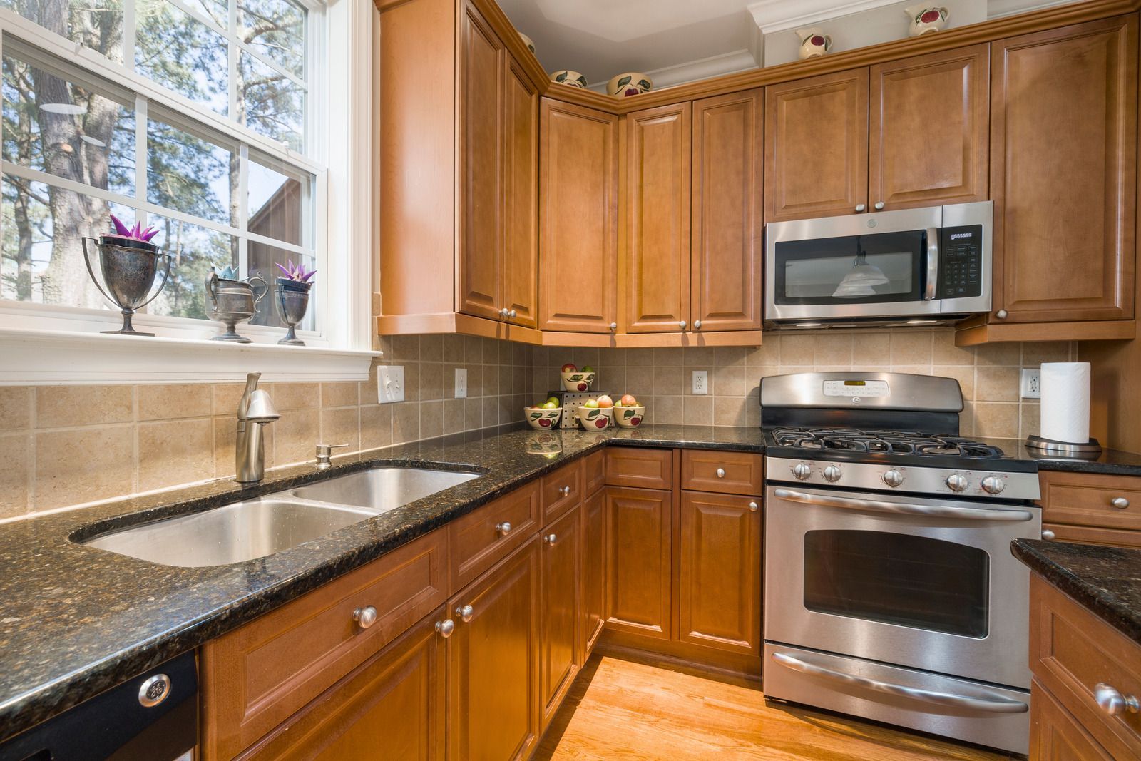Kitchen with wooden cabinets, stainless steel appliances, black countertop, and a window.