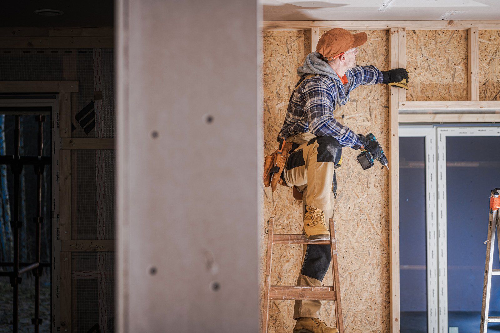 Person on a ladder, building a wall with wooden boards; interior construction site.