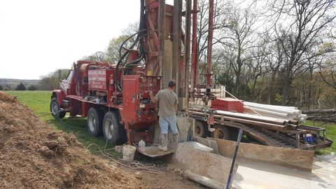 A man is standing next to a drilling rig in a field.