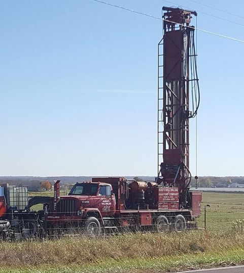 A red truck is parked in a field next to a large drill