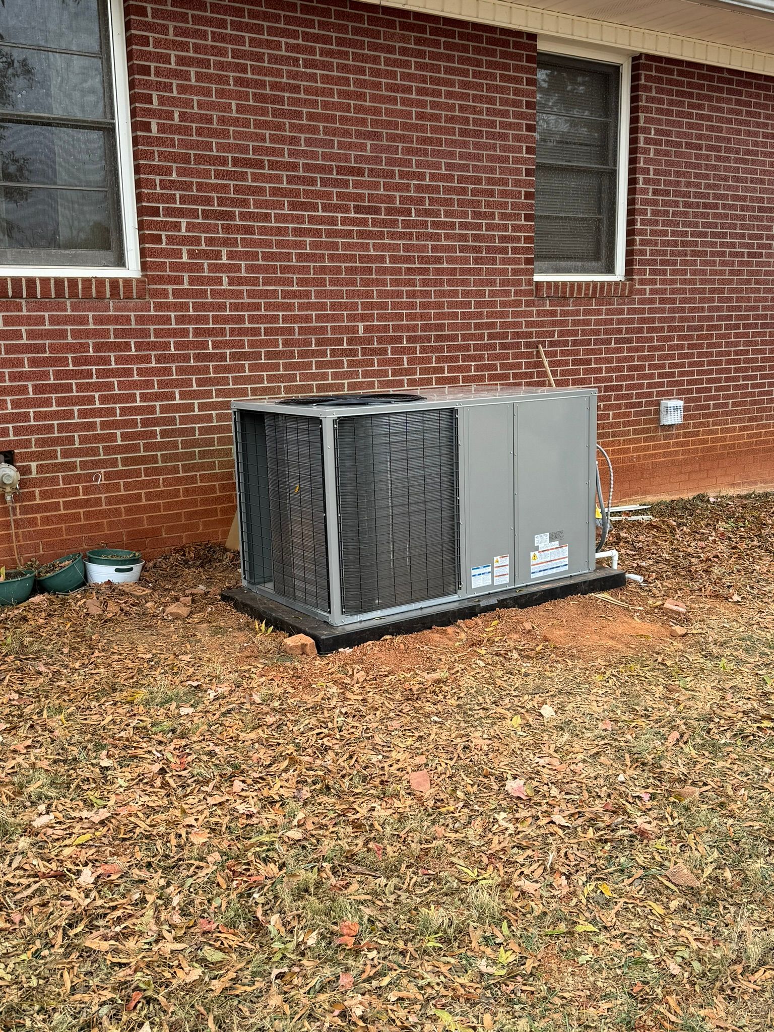 A large air conditioner is sitting in front of a brick house.