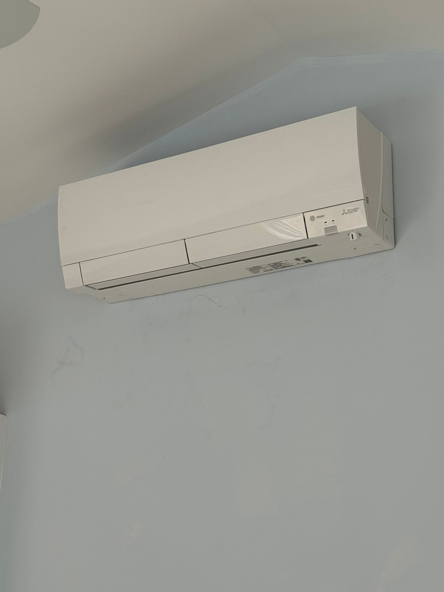 A white air conditioner is hanging from the ceiling on a wall.