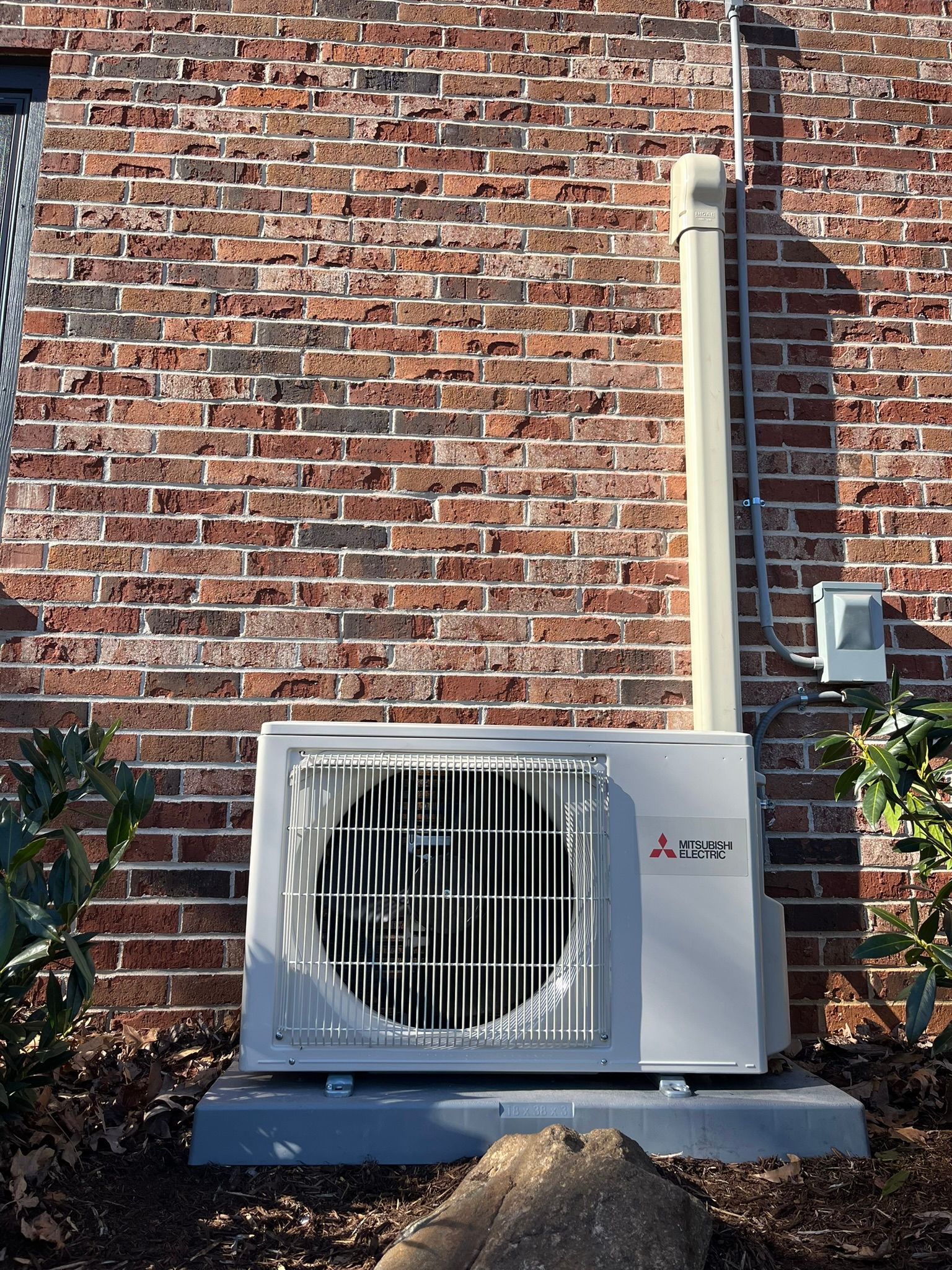 A mitsubishi air conditioner is mounted on the side of a brick building.