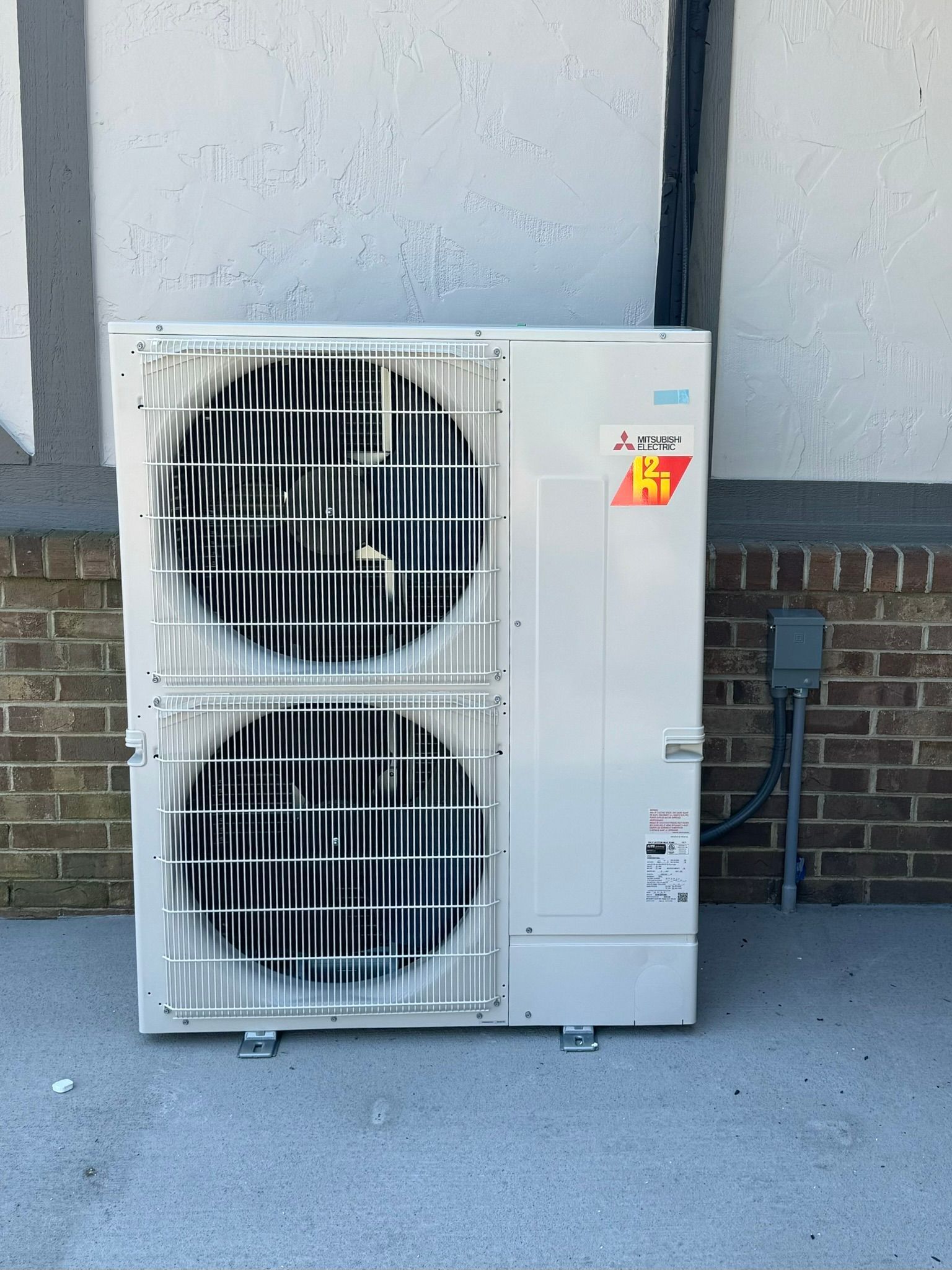 A large air conditioner is sitting on the side of a brick building.
