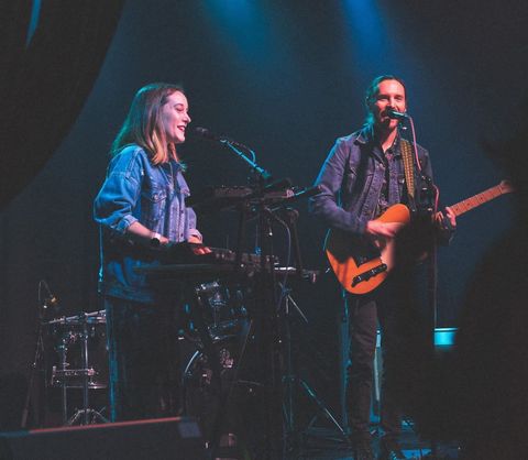 A woman and man singing into a microphone while playing a guitar