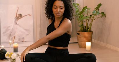 A woman is sitting on the floor in a lotus position with her eyes closed.