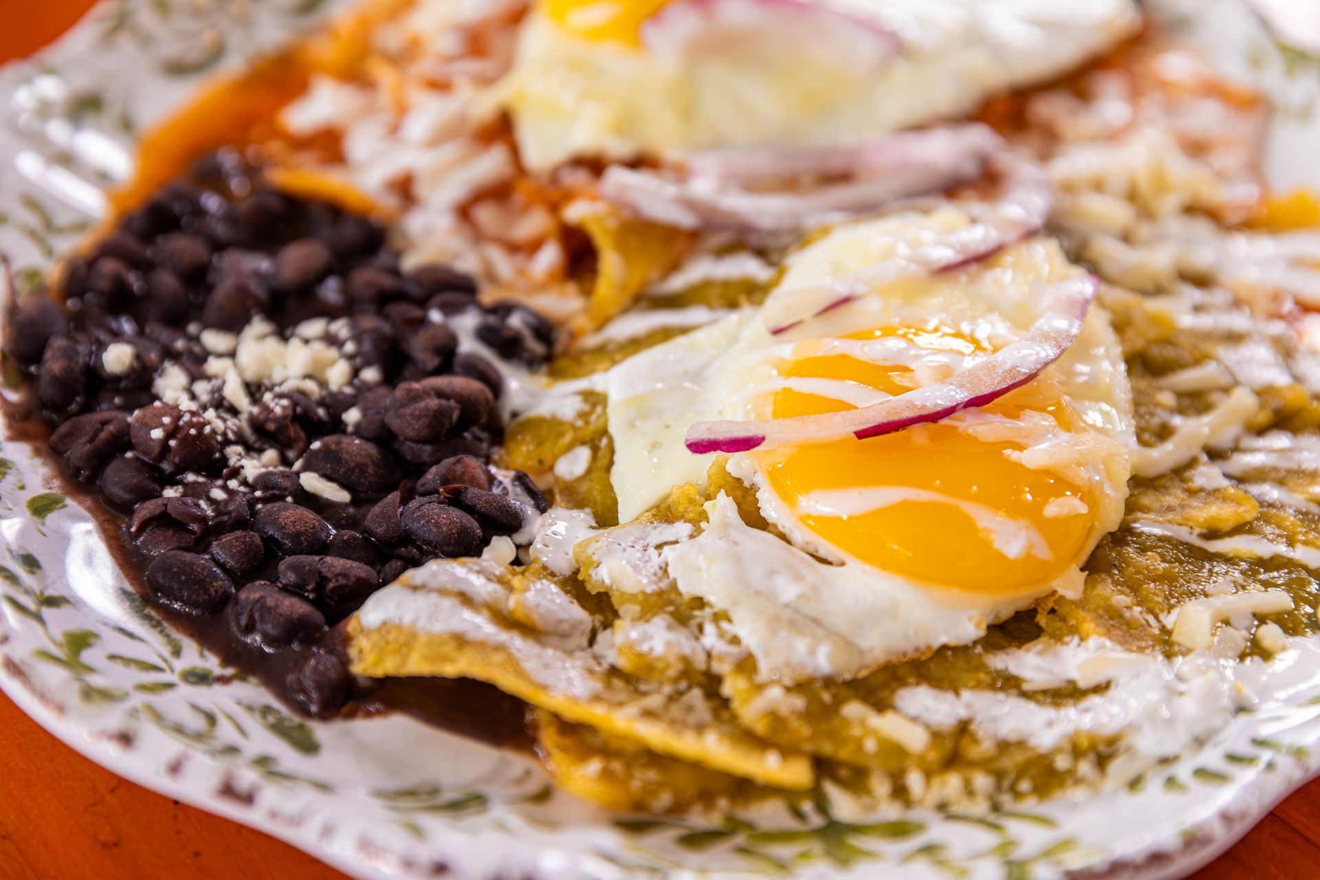 Chilaquiles with eggs, black beans, and toppings on a decorated plate.