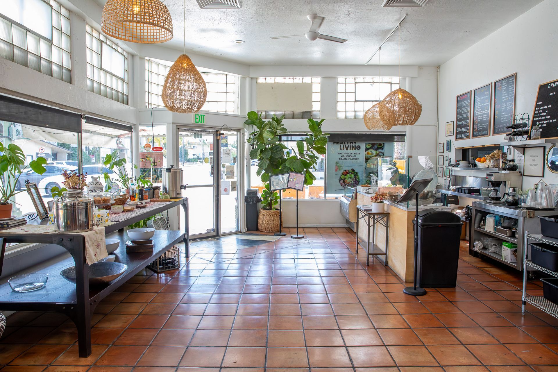 Interior of a cafe with large windows, potted plants, and tables displaying food and products.