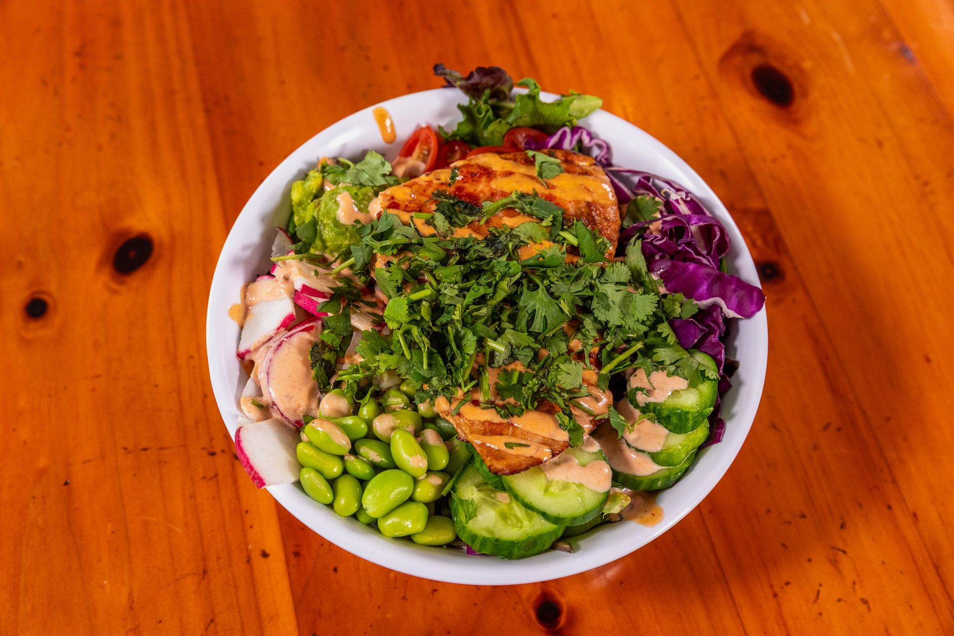Bowl of colorful salad with chicken, vegetables, and dressing on a wooden table.