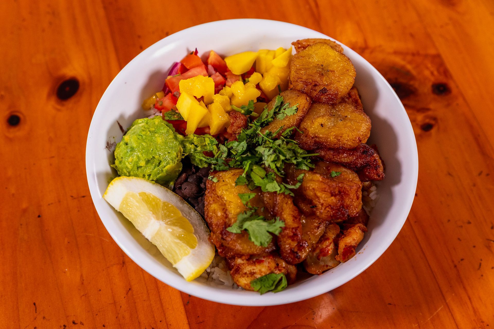 Bowl of food with fried plantains, guacamole, mango salsa, and lemon.