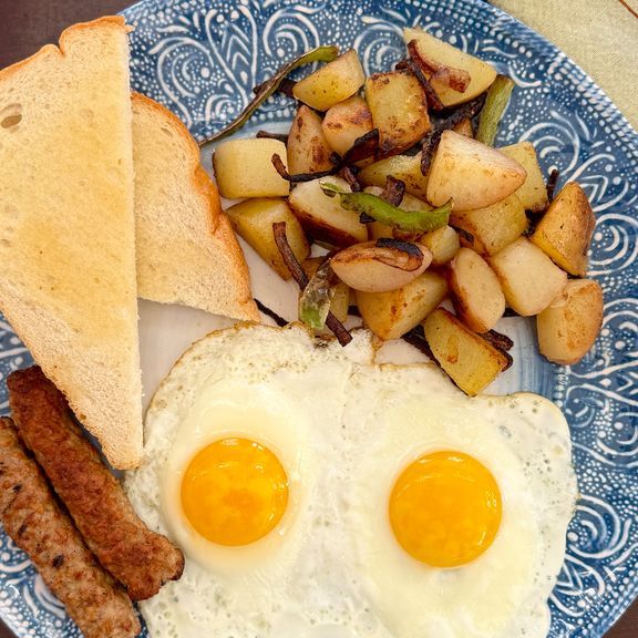 Breakfast plate with fried eggs, toast, sausage, and potatoes.