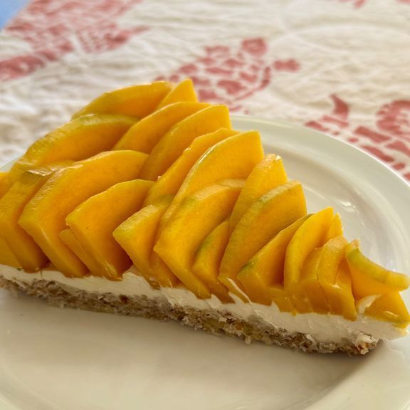 Mango tart slice on a white plate, with a crumb crust, creamy filling, and layered mango slices.
