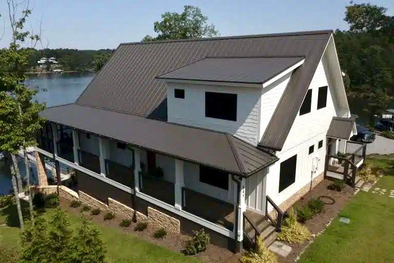 An aerial view of a white house with a black roof next to a lake.