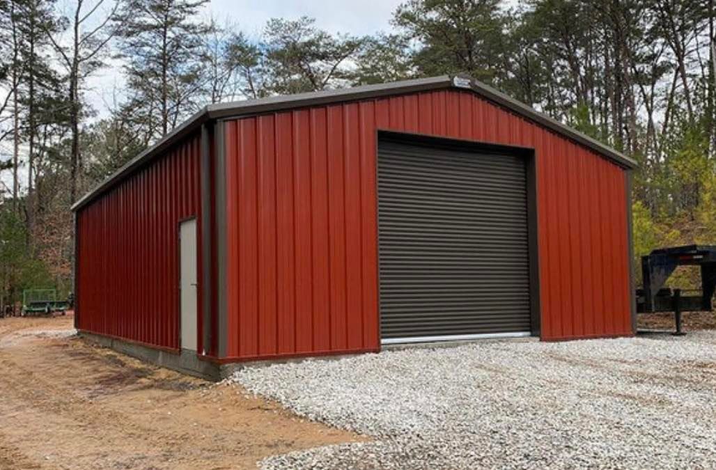 A red metal building with a garage door is sitting on top of a gravel road.