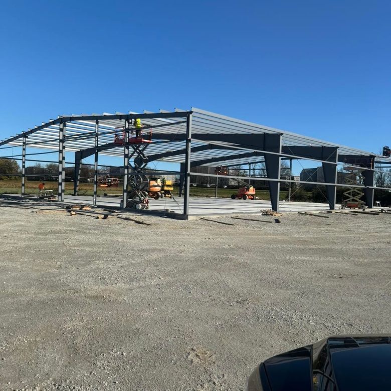 A large metal structure is being built in a gravel lot