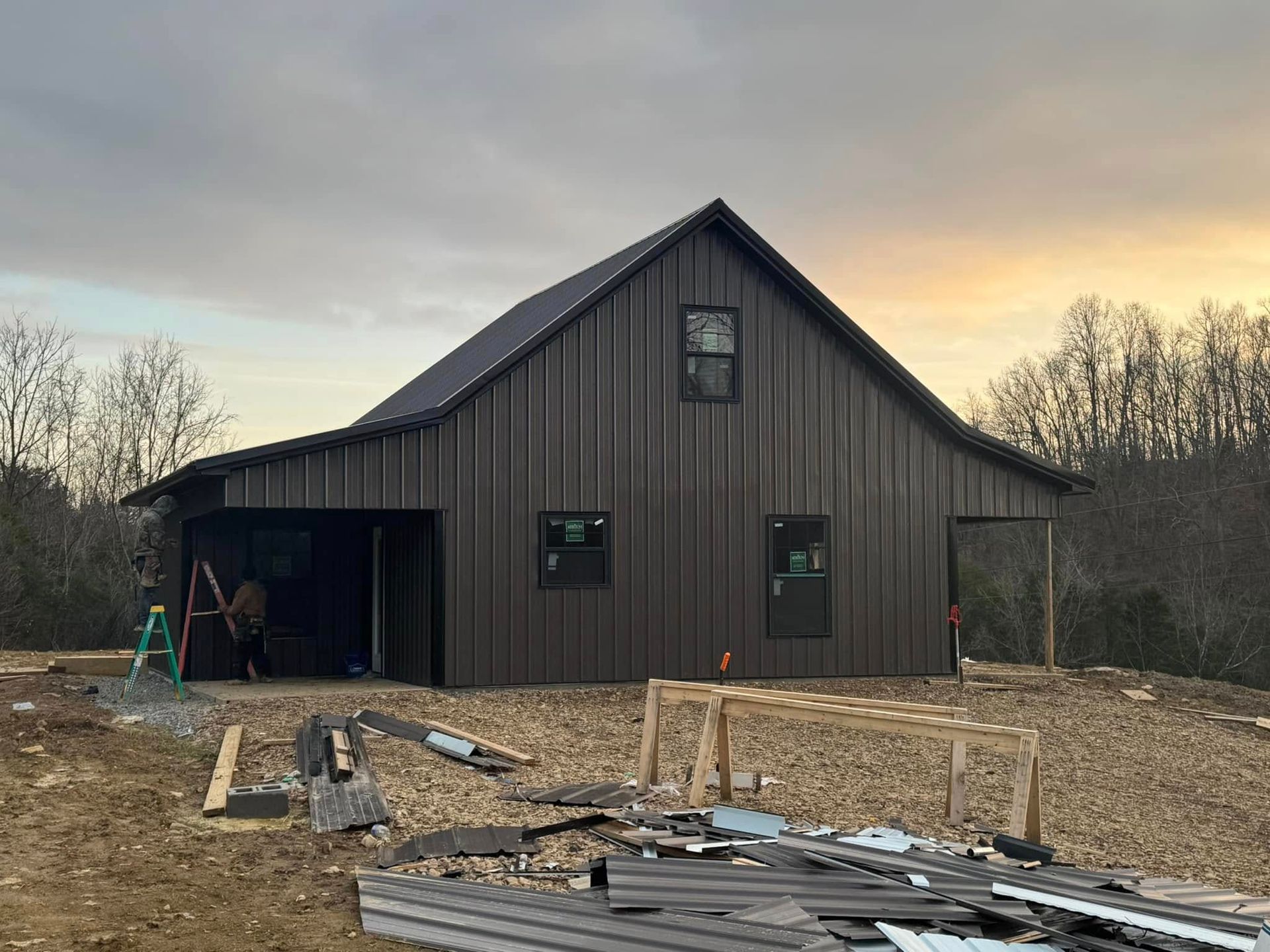 A large black barn is being built on top of a dirt hill.