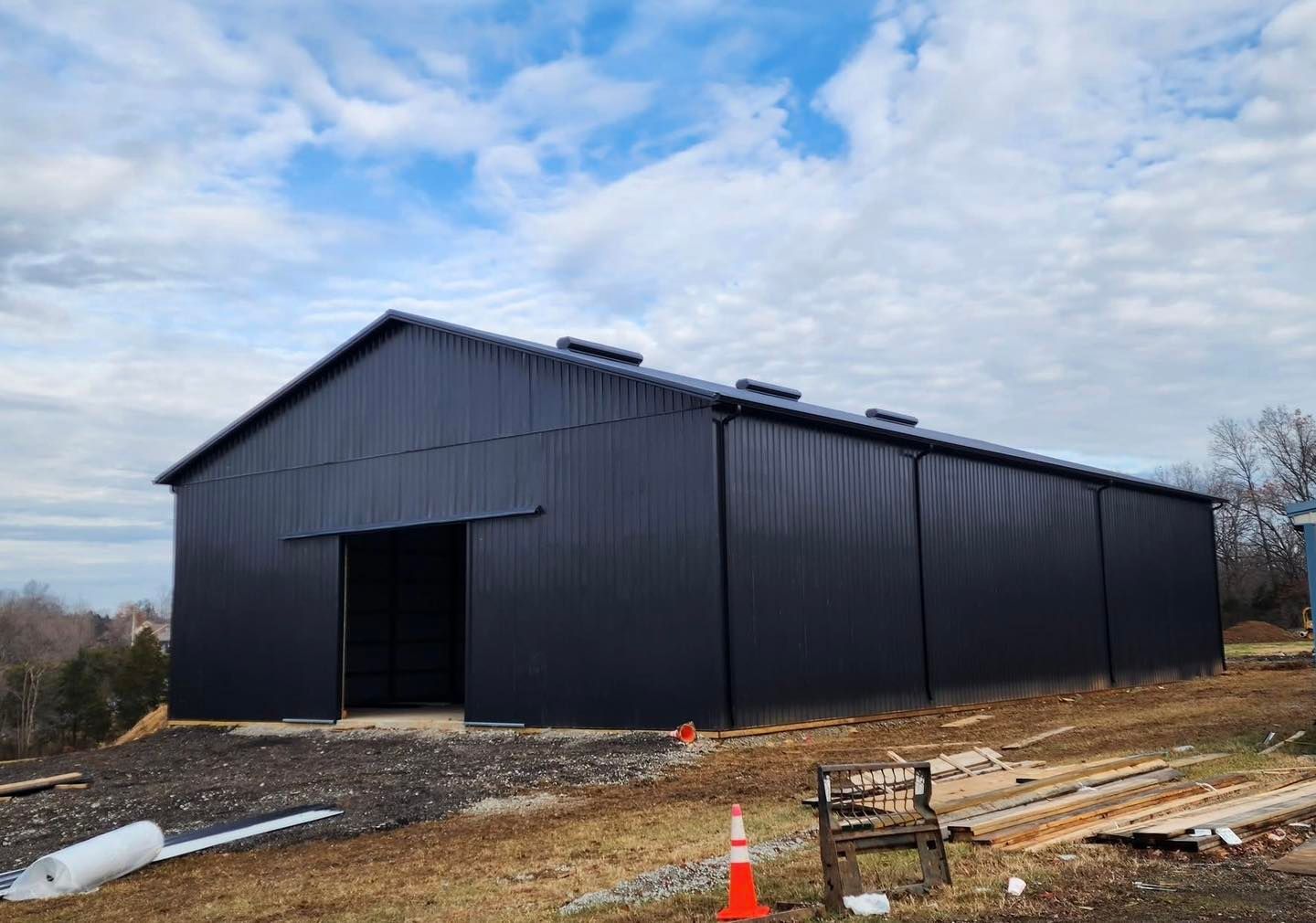 A large black metal building is being built in a field.