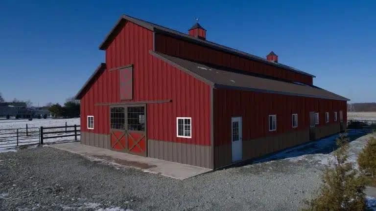 A large red barn is sitting in the middle of a snowy field.