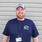 A man wearing a hat and a name tag is standing in front of a wall.