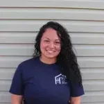 A woman in a blue shirt is standing in front of a siding wall.