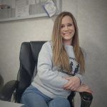A woman is sitting in an office chair and smiling.