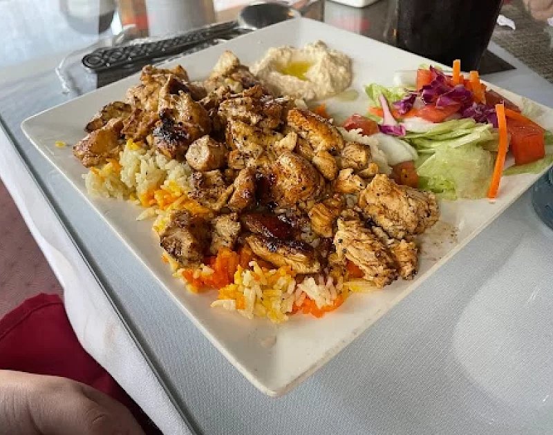A white plate topped with chicken , rice , and vegetables on a table.