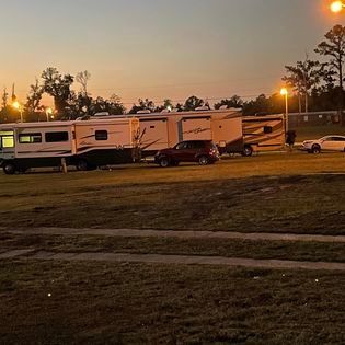 A row of rvs are parked in a grassy field at night.