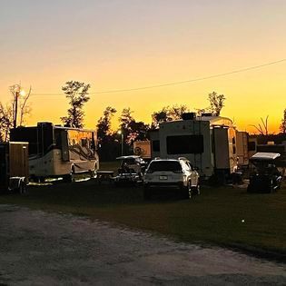 A group of rvs are parked in a field at sunset.