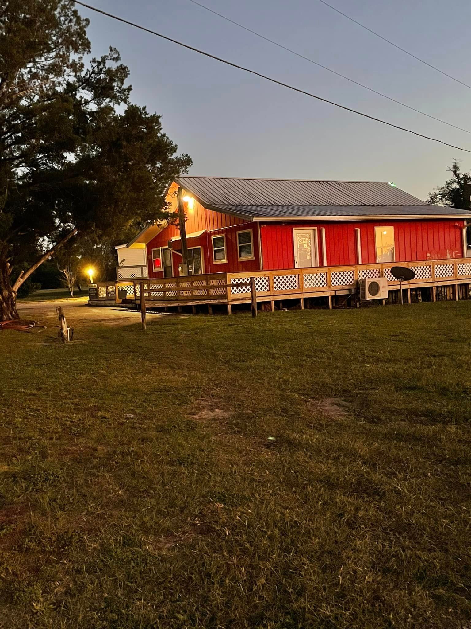 A red house is sitting in the middle of a grassy field.