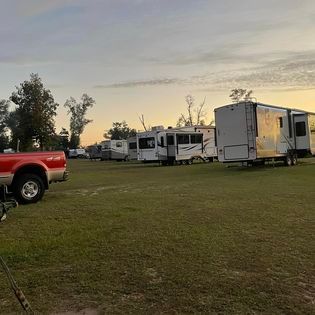 A row of rvs are parked in a grassy field next to a red truck.