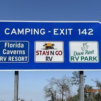 A blue sign that says `` camping exit 142 florida caverns rv resort stay n go rv dove rest rv park ''