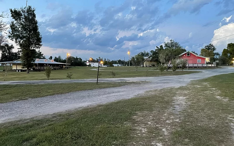 A dirt road going through a grassy field with a red barn in the background.